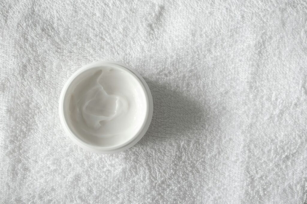 Moisturizer cream or body lotion on white bathroom towel background